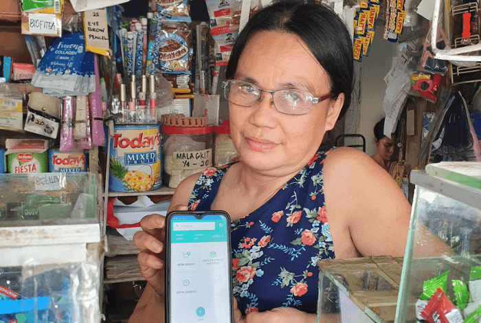 Woman in glasses holding smartphone with a blue app in a small store.