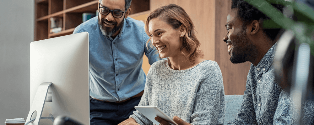 Three diverse colleagues smiling while collaborating and looking at a computer screen.