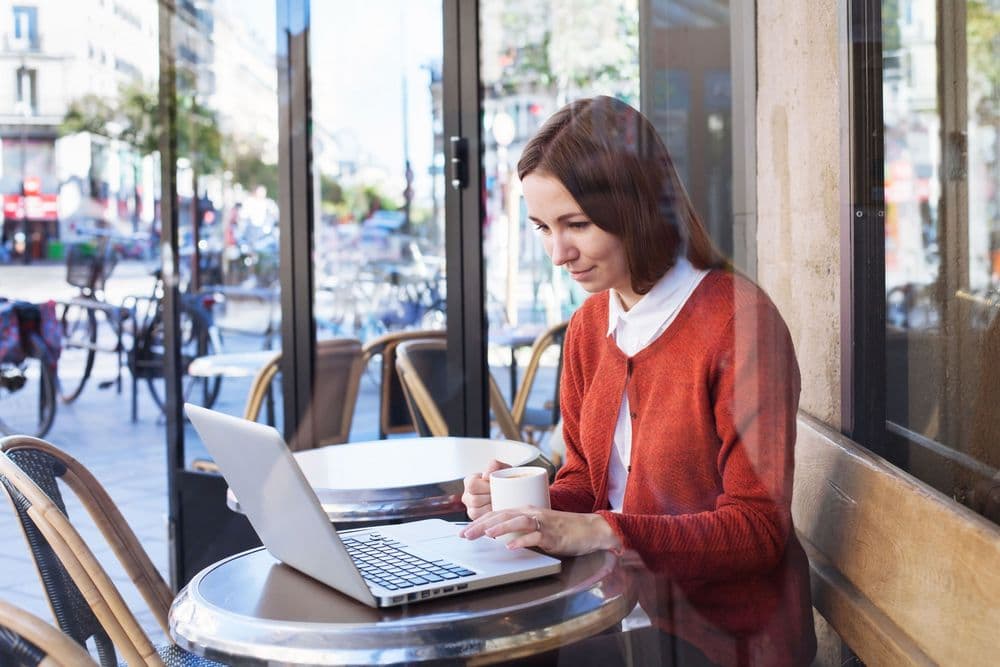 Woman in red cardigan working on laptop at an outdoor Parisian cafe.