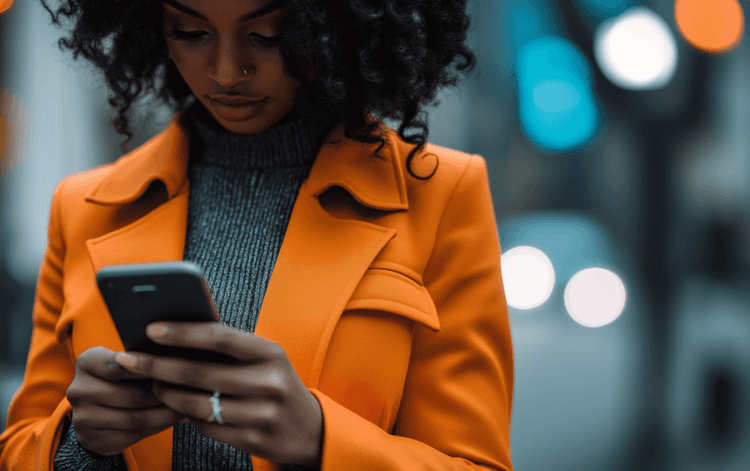 Young woman in orange coat uses smartphone, blurred city lights in background.