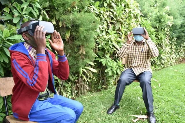 Two men wearing VR headsets sit outdoors in a garden, experiencing virtual reality.