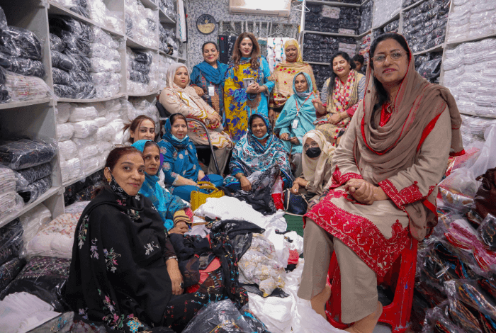 Group of women smiling among stacks of textiles in a bustling workshop.