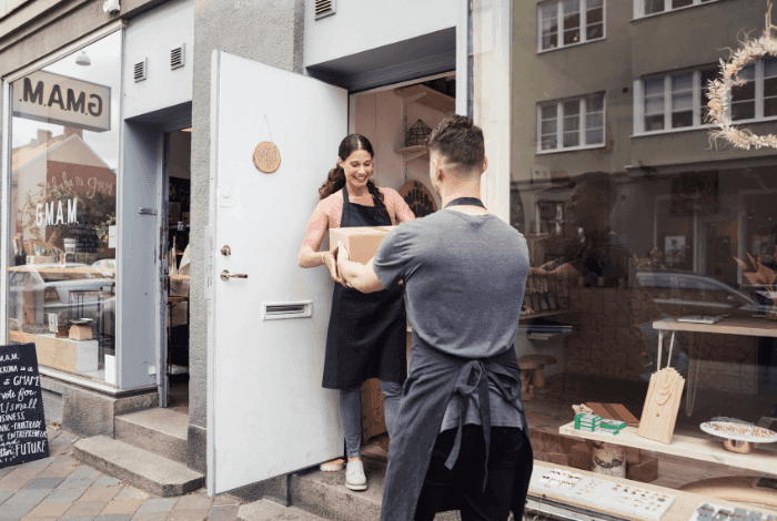 A woman hands a package to a man in aprons at a shop's open doorway.