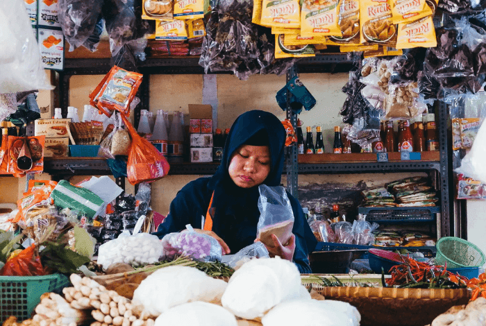 Woman in hijab packaging spices and produce at a bustling market stall.