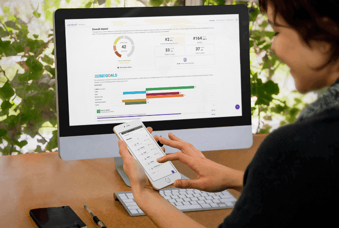 Woman analyzing data on a desktop computer and a smartphone with dashboard interfaces.