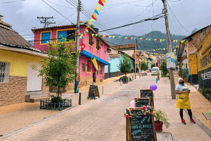 Vibrant street scene in Bogota with colorful houses, festive flags, and a street vendor.