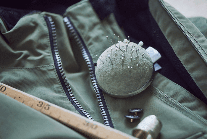 Sewing essentials: a pin cushion with pins, wooden ruler, and thimble on green fabric.