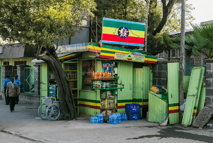 A vibrant green and yellow kiosk with an Ethiopian flag selling drinks and snacks on a street.