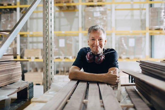 Smiling man in a workshop with wooden planks and industrial shelving.