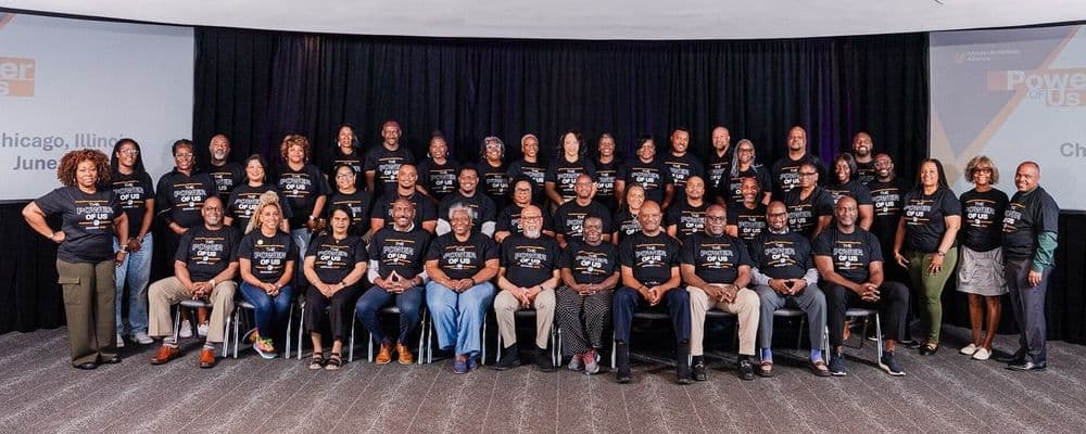 Diverse group of colleagues in black logo shirts gather for a team photograph indoors.