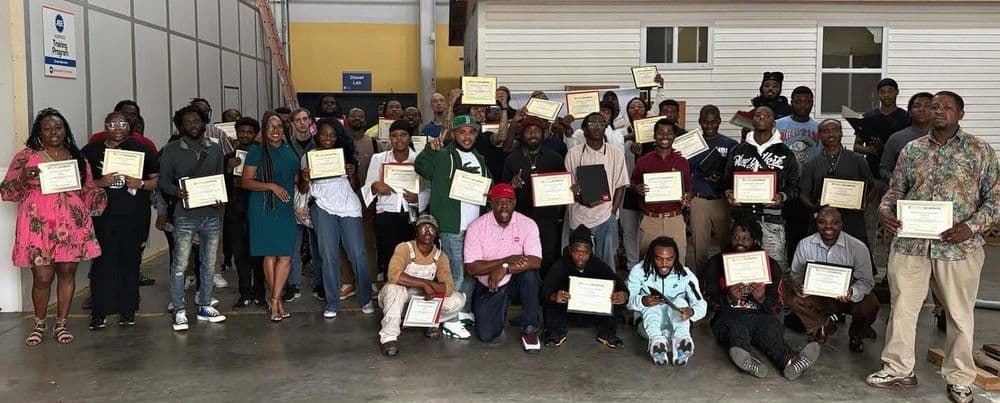 Diverse group of adults proudly holding their certificates indoors, celebrating an achievement.