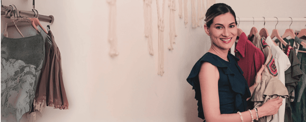 Smiling woman holding clothes, standing by a rack with various garments.