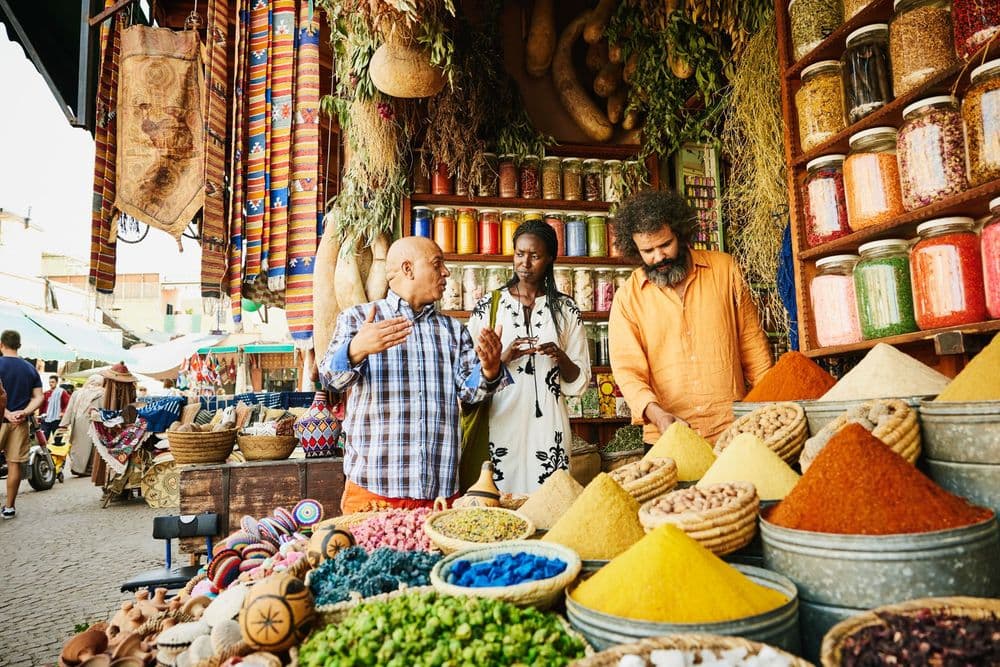 People browsing vibrant spices and goods at a colorful outdoor market stall.