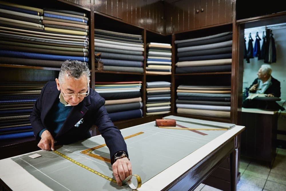 Experienced tailor meticulously measures fabric on a large cutting table in a traditional workshop.