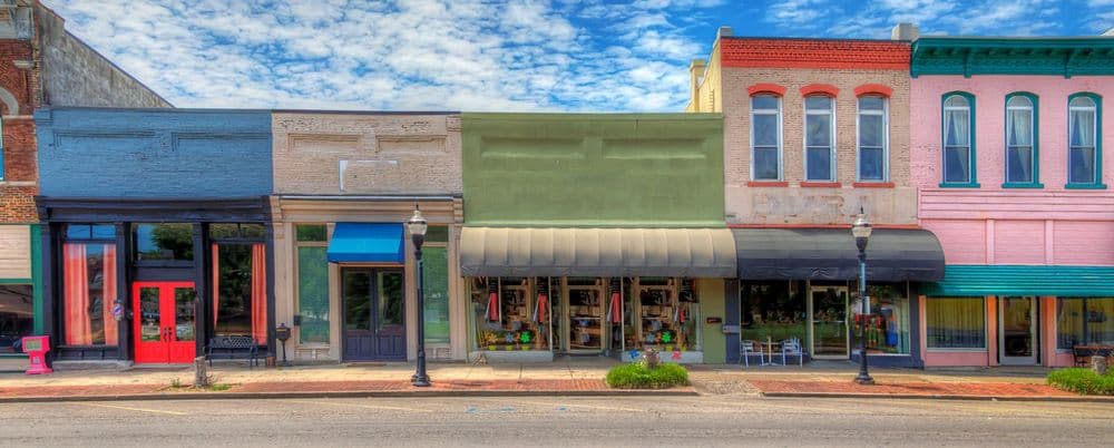 Vibrant historic storefronts with colorful facades and awnings line a street under a cloudy sky.