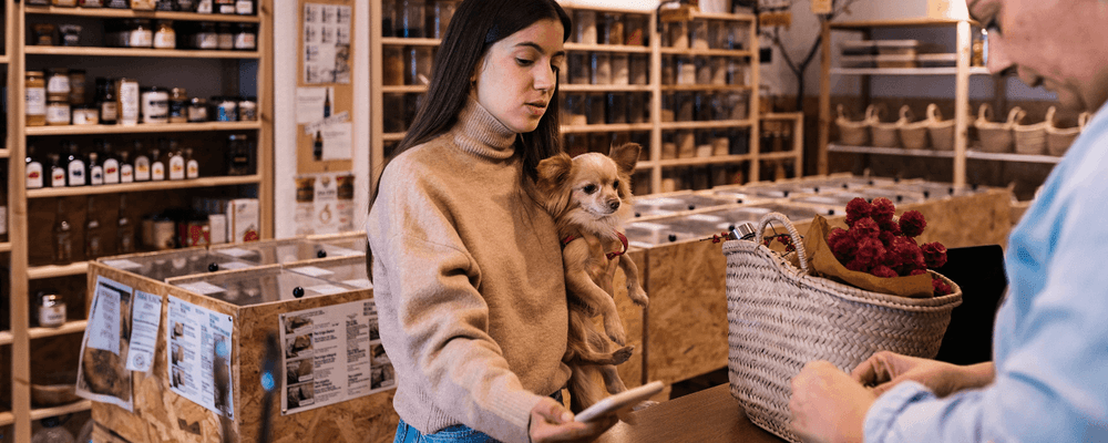 Young woman holding a small dog while looking at her phone in a modern store.