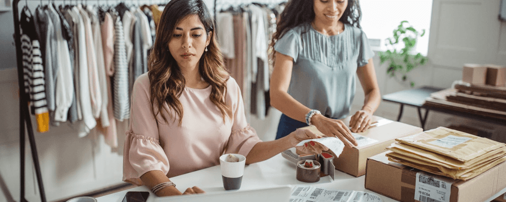 Two women diligently preparing packages and managing orders for their online retail business.