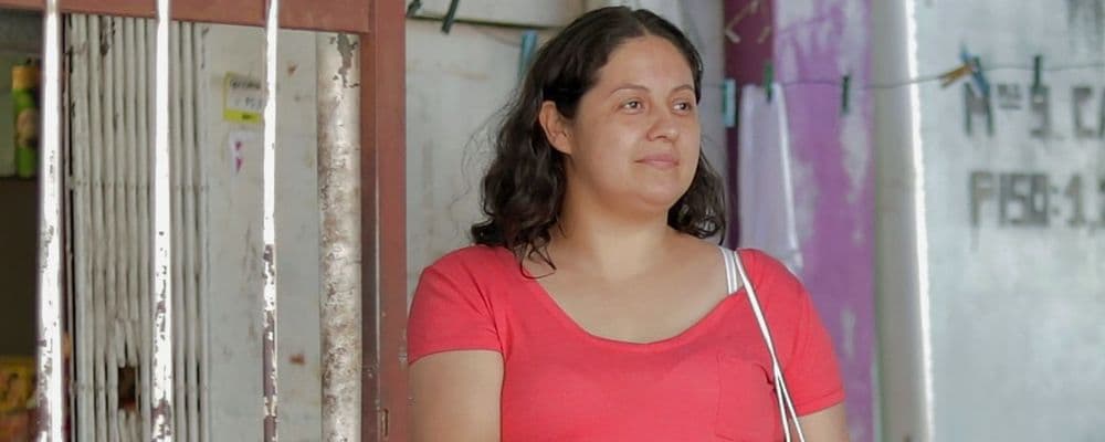 A woman in a red shirt with dark hair looks right, against a blurred background.