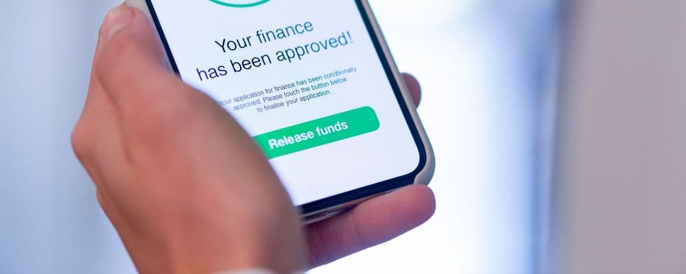Hand holding a smartphone displaying "Your finance has been approved!" and a "Release Funds" button.