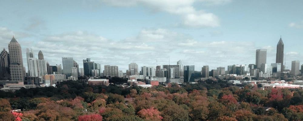 Urban skyline towering over a park with vibrant red and orange autumn foliage.