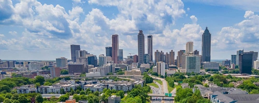 A panoramic view of Atlanta's modern skyline with numerous skyscrapers under a partly cloudy sky.