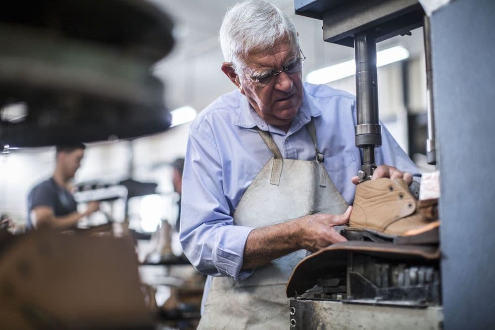 Experienced craftsman precisely shapes leather using industrial machinery in a well-lit workshop.