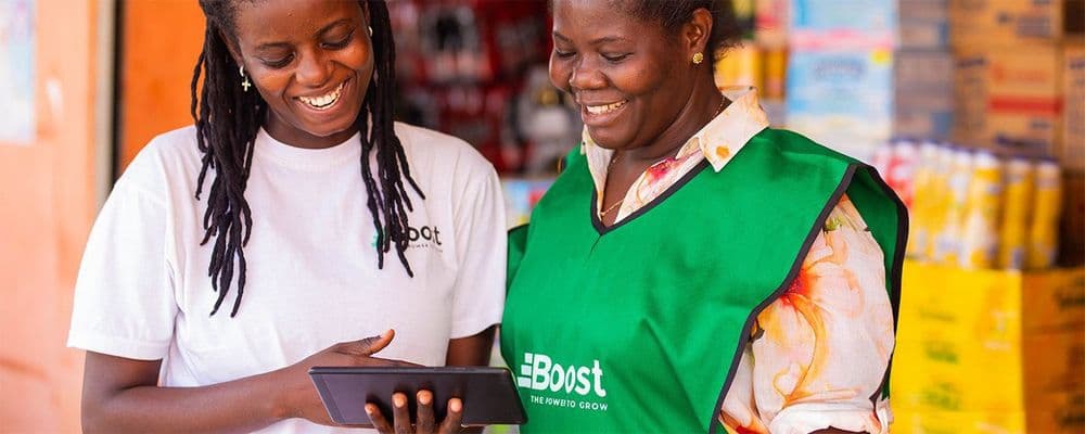 Two women, one in a Boost apron, smiling and looking at a tablet.