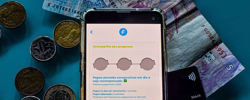 Smartphone displaying a payment app surrounded by Brazilian coins, banknotes, and a credit card.