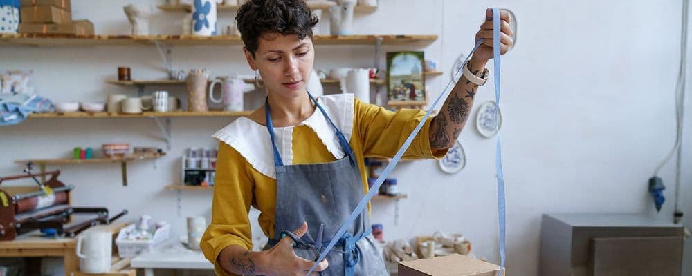 Woman in apron carefully cuts a long strip of material in a pottery workshop.