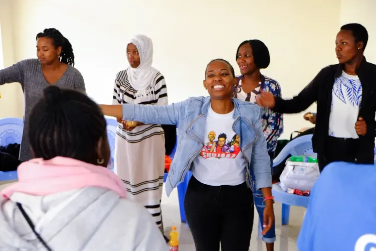 A smiling young woman actively leads a group of women in an interactive session.