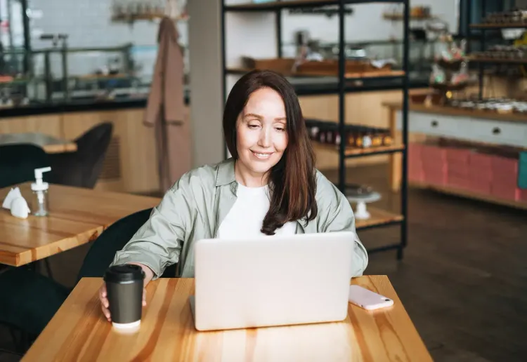 Woman smiling while working on a laptop at a cafe table.