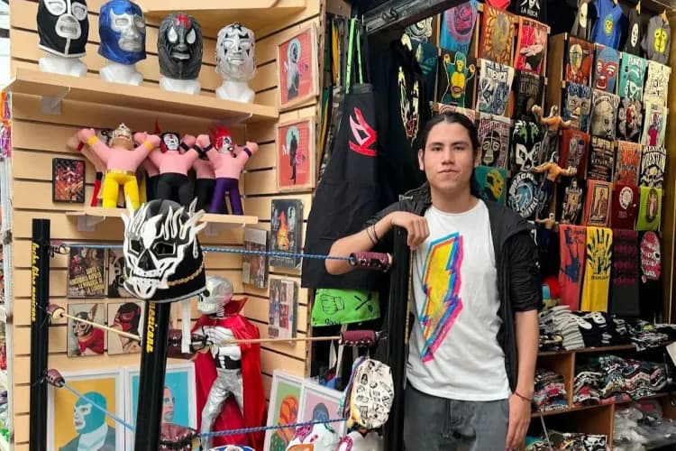 A young man stands in a shop filled with colorful Lucha Libre wrestling masks and figures.