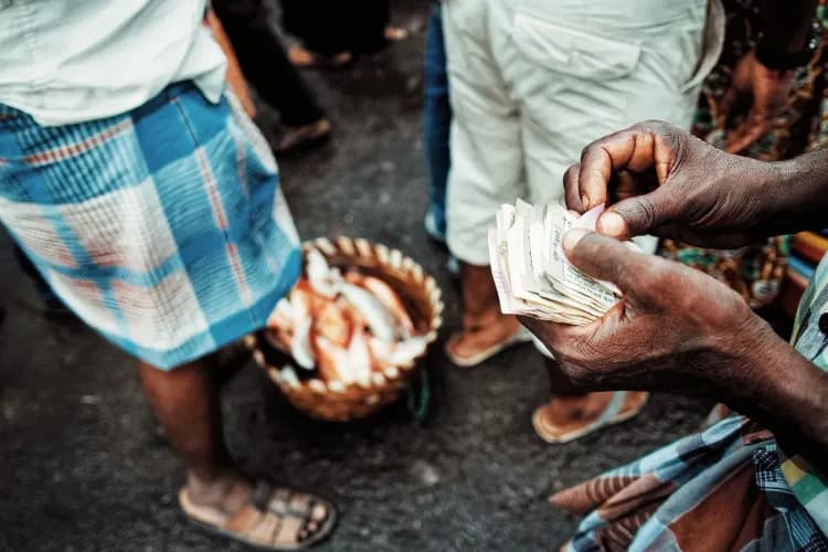 Close-up of hands counting a stack of paper currency notes at an outdoor market.