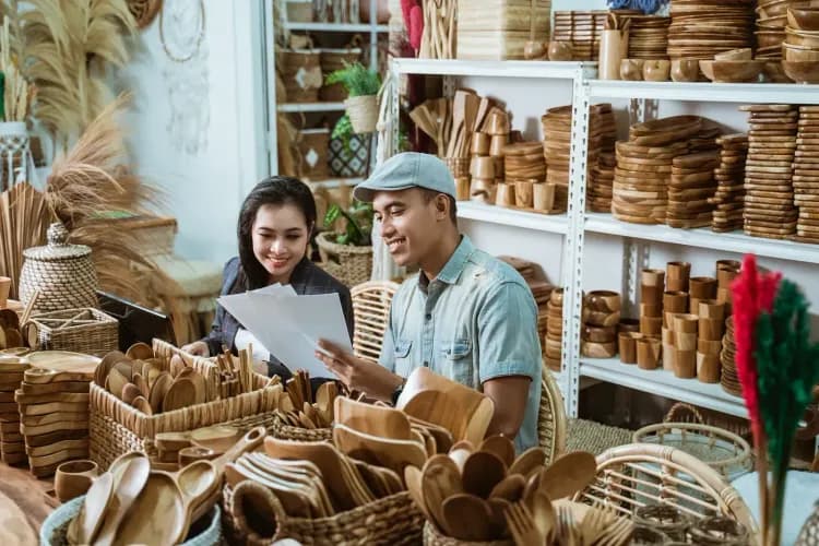 Two smiling small business owners review documents surrounded by handmade wooden crafts.