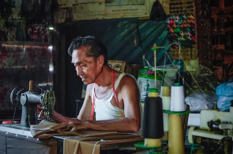 A focused man sews fabric on a vintage sewing machine in a cluttered workshop.