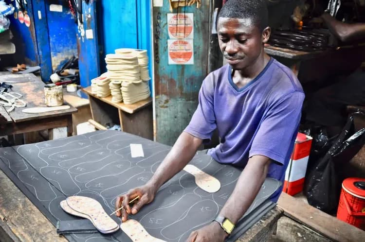 Man cutting shoe soles from material in a bustling workshop.