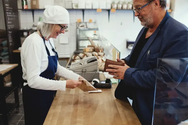A smiling barista hands a packaged item to a customer at a cafe counter.