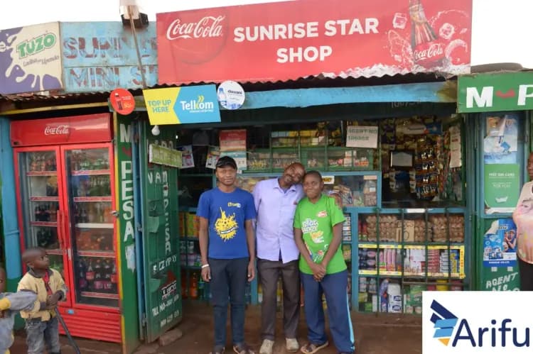 Three men stand proudly in front of their small, brightly painted "Sunrise Star Shop".