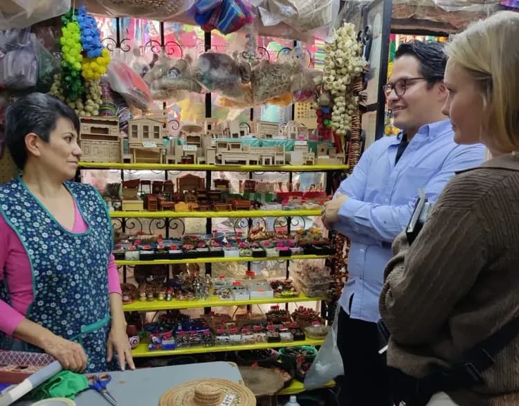 Shop owner conversing with two customers amidst shelves of handmade goods in a market.