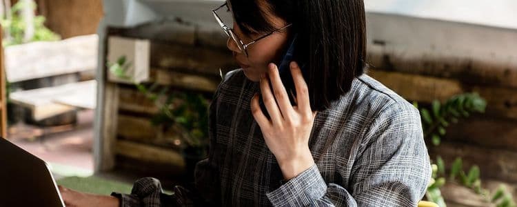 Woman with short dark hair and glasses talking on a phone, with a laptop nearby.
