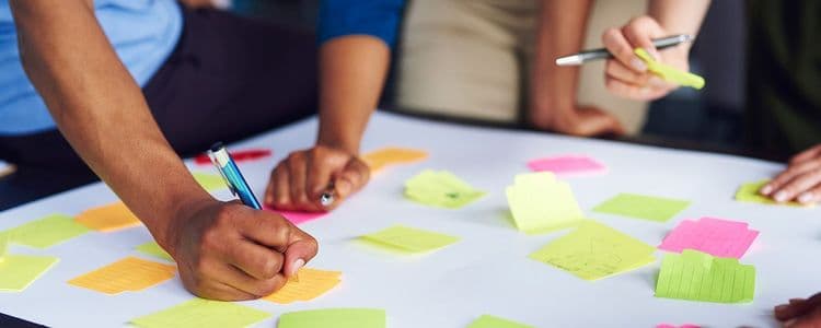 Several people collaborate, writing notes on colorful sticky notes arranged on a white table.