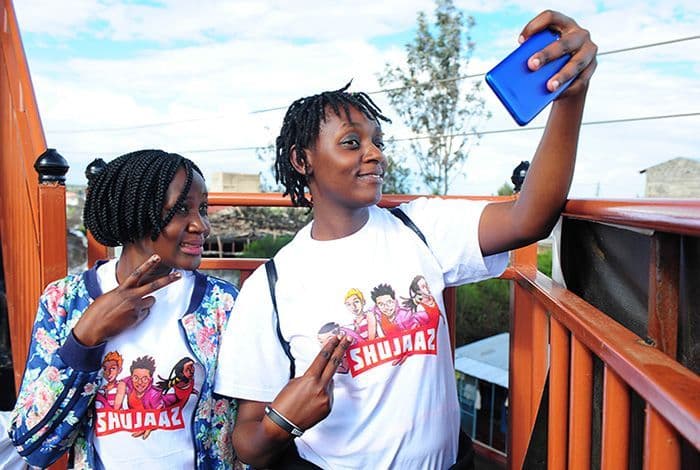 Two young people in matching white t-shirts pose for a selfie on an outdoor bridge.