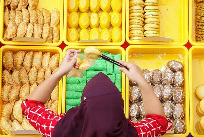 Person picking green sweets from yellow tray among many other diverse pastries.
