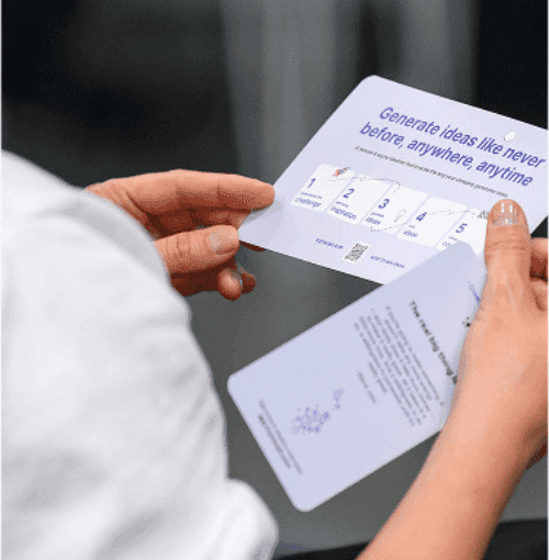 Person holding a purple folded card displaying 'Generate ideas like never before, anywhere, anytime.'
